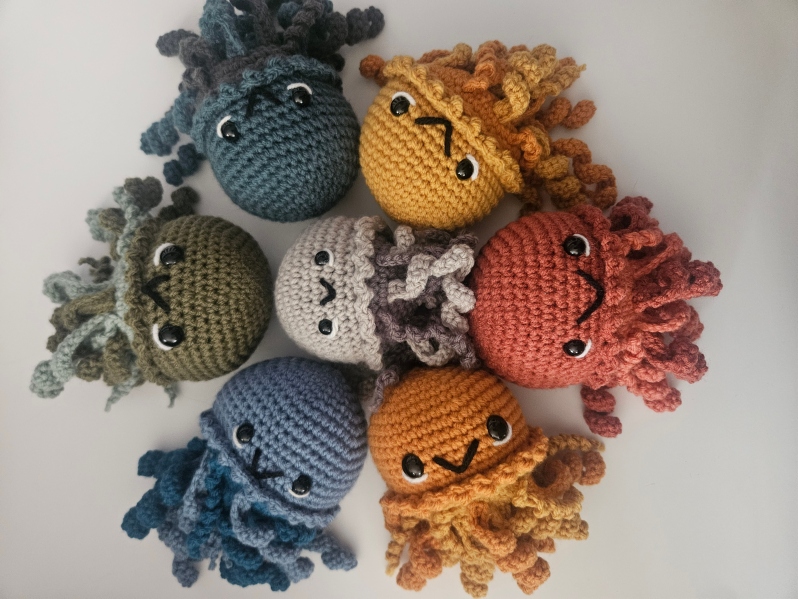 Product Description: Amigurumi Jellyfish by Casey Lucas</br>Apt2Designs</br></br>Medium size and whimsical jellyfish. Available is different colors. Great gift for family and friends</br></br>Materials Used: Yarn, Polyfil, Safety Eyes</br>approximately 4w x 10h x 5d inches</br></br>Artist Statement: Crochet is one of my favorite mediums for artistic expression, where yarn and a hook become the tools through which I craft whimsical characters and imaginative worlds. With each stitch, life is given to these soft sculptures, transforming simple materials into endearing creatures. My work in Amigurumi crochet is a testament to the power of handmade artistry, as each piece has their own unique personality and charm. Through this craft, I seek a sense of wonder, joy, and nostalgia in those who encounter my creations, inviting them to embrace the magic of the handmade and the infinite possibilities of yarn.</br></br>Amigurumi is a Japanese crochet or knit technique used to create small, stuffed animals, dolls, and other cute objects, often with a distinct, whimsical style. The word "Amigurumi" is a blend of two Japanese words: "ami" (meaning knitted or crocheted) and "nuigurumi" (meaning stuffed doll). Amigurumi pieces are typically worked in the round and characterized by their adorable, oversized heads and tiny bodies, making them popular among crafters for their charm and versatility in creating soft, decorative items.</br></br>Bio: Casey Lucas is a versatile artist with a background in both dance and visual arts. She earned her Bachelor of Fine Arts (BFA) in Dance from Mason Gross School of the Arts and a Master of Fine Arts (MFA) in Art - Ceramics from Kean University. Casey's artistic journey spans various creative mediums, including Amigurumi crochet and ceramics, through which she brings her unique vision to life. After living in New York City for over a decade, she currently resides in the picturesque town of Princeton, New Jersey. Casey shares her life with her husband and two children, drawing inspiration from the town's historic charm. Her work beautifully combines the tactile and visual arts, creating a seamless fusion of movement, texture, and form. Whether through the fluidity of dance or the intricacies of crochet and ceramics, Casey's artistry is a testament to her unwavering commitment to the creative process. Beyond her artistic pursuits, Casey is a recent breast cancer survivor, showcasing incredible resilience and strength throughout her personal journey. She has chosen to use her art as a force for good, dedicating a portion of her sales to support cancer research. Her work not only embodies creativity and passion but also carries a profound message of hope and determination.</br></br>$18</br></br>*Price is subject to sales tax</br></br>Item Number: CL36</br> Amigurumi Jellyfish by Casey Lucas